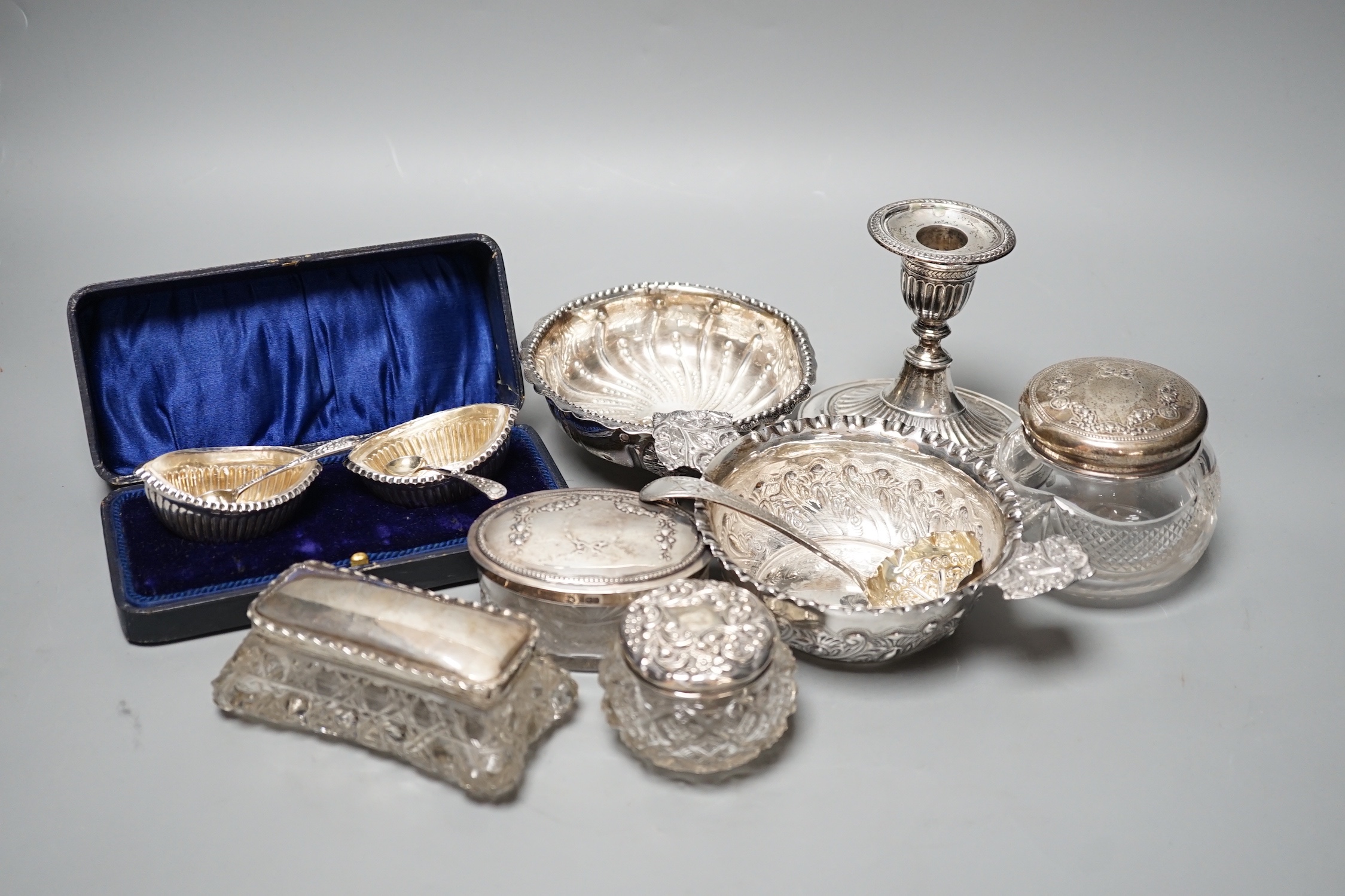 A Victorian repousse silver two handed bowl, one other silver bowl, a silver sifter spoon, four silver mounted glass toilet jars, a silver dwarf candlestick and a cased pair of silver salts.